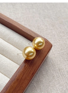 Detail view of round golden pearl earrings on a premium wooden jewelry display tray