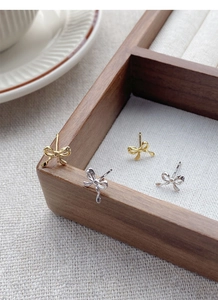 Close-up of S925 bow stud earrings in gold and silver on a wooden jewelry display