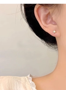 Detailed close-up of a model wearing a gold eight-pointed star stud earring with a small zircon