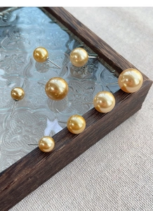 Macro shot of gold round pearl earrings in various sizes on a decorative glass tray