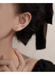 Detail view of dainty silver bow earrings worn by a model in a minimalist style