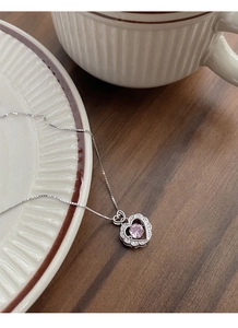 Detail shot of a S925 sterling silver heart necklace with a pink center stone on a ceramic tray