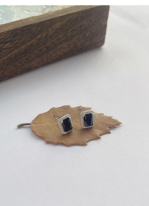 Détail de boucles d'oreilles carrées en zircon noir avec halo sur fond de feuille naturelle