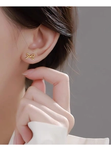 Close-up of elegant gold bow stud earring made of twisted metal wire on model