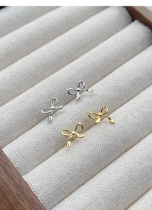 Macro shot of silver and gold bow earrings displayed in a soft cream jewelry box