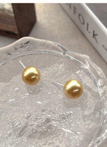 Detailed view of high-lustre round golden pearl stud earrings on a cracked glass texture