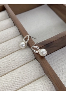 Close-up of S925 sterling silver geometric pearl earrings on a wooden jewelry box