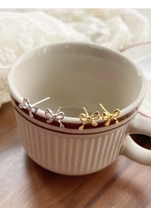 Close-up of gold and silver bow stud earrings on a vintage cup rim with lace