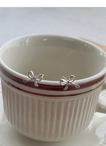 Detailed macro shot of elegant S999 silver bow earrings on a ceramic cup rim