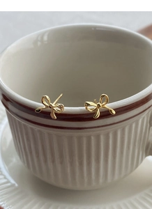 Detailed view of elegant gold bow stud earrings displayed on a white ceramic cup rim