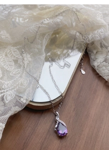 Macro detail of purple teardrop crystal pendant with silver chain on lace background