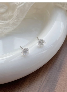 Detailed view of iridescent camellia flower stud earrings on white ceramic tray