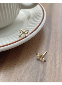 Detail of golden bow stud earrings on a ceramic dish with soft natural lighting