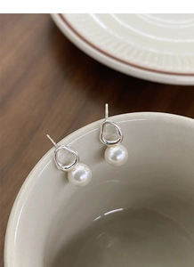 Close-up of S925 silver irregular geometric earrings with elegant white pearls on ceramic