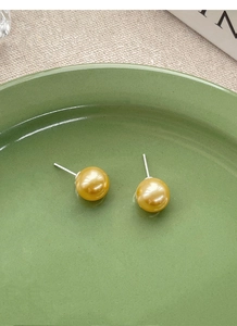 Detailed macro view of elegant golden pearl earrings with S925 silver pins on ceramic tray