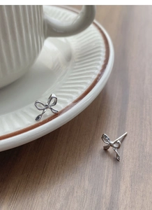Detail view of silver bow stud earrings resting on a white ceramic cup edge