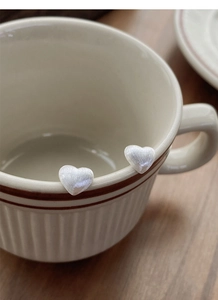Détail de boucles d'oreilles cœur en argent brossé mat posées sur une tasse de style vintage