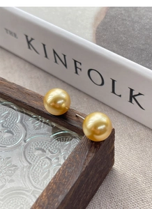 Close-up of golden round pearl earrings on a vintage glass surface with a book
