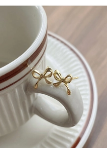 Close-up of golden bow-shaped S999 silver stud earrings on a vintage coffee cup handle