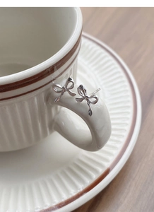 Close-up of S999 sterling silver bow knot stud earrings on a ceramic cup handle