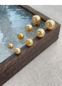 Macro shot of assorted sizes gold pearl stud earrings on a textured vintage tray