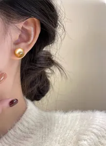 Close-up of elegant 12mm golden pearl stud earrings on model with cozy knit sweater