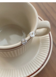 Detailed view of hollow rose-shaped silver earrings displayed on a cream ceramic cup
