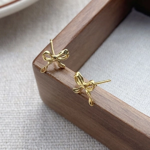 Elegant gold bow earrings made of S999 sterling silver on a rustic wooden display stand
