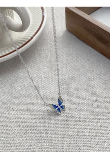 Detailed macro view of S925 enamel butterfly necklace on a grey linen background