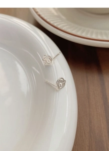 Macro shot of silver rose stud earrings with minimalist hollow design on white ceramic
