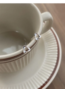 Detailed view of silver knot triangle stud earrings hanging on a vintage cup rim