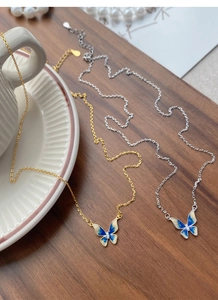 Detail of silver and gold butterfly necklaces with blue enamel and cubic zirconia on wood