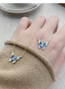 Detail of blue enamel butterfly pendant necklace wrapped around finger on hand