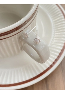 Macro view of sterling silver daisy stud earrings hanging on a ceramic cup handle