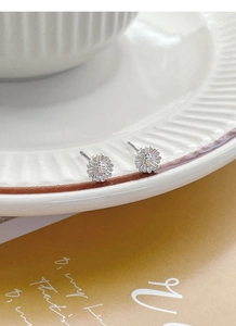 Close-up of minimalist S999 sterling silver daisy stud earrings on ceramic dish