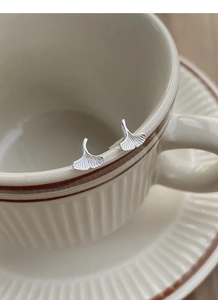 Detailed close-up of silver ginkgo leaf stud earrings hanging on a vintage cup rim