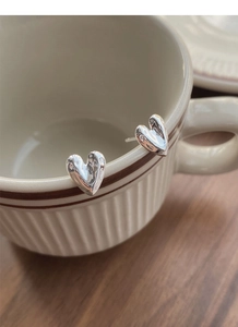 Detail of S999 silver heart stud earrings with textured finish on a coffee cup rim