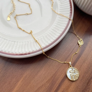 Collier en argent S925 doré avec pendentif Fu en nacre sur une assiette en porcelaine