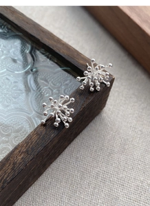 Macro shot of silver firework stud earrings placed on a decorative glass tray