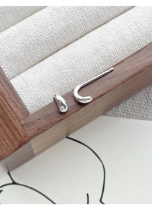 Detailed close-up of polished S999 sterling silver C-shaped stud earrings on a wooden box