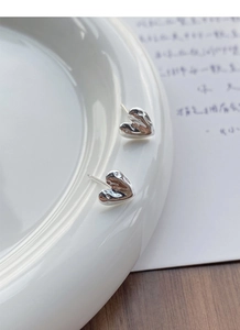 Macro view of minimalist textured silver heart earrings on a ceramic plate