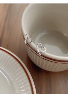 Detailed view of minimalist S999 sterling silver hollow heart earrings hanging on a cup