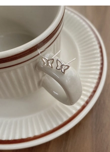 Detailed view of butterfly-shaped silver stud earrings hanging on a vintage cup