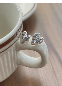 Macro detail of S999 silver heart stud earrings with liquid metal texture on a ceramic cup