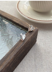 Detailed macro view of S999 sterling silver heart studs with liquid metal texture on wood