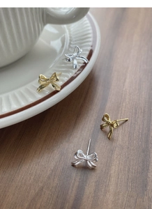 Détail de boucles d'oreilles nœuds dorées et argentées sur céramique blanche