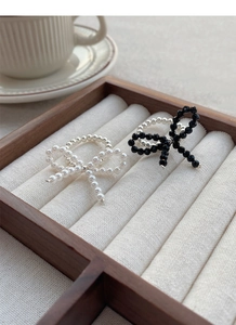 Detailed view of elastic silver bow rings with white pearls and black faceted beads