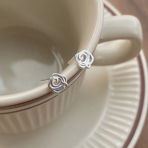 Minimalist S999 silver hollow rose stud earrings displayed on a vintage ceramic cup rim