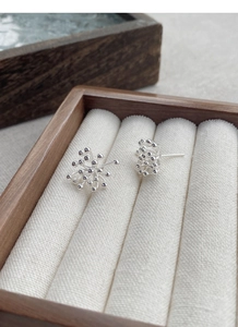 Macro shot of S925 sterling silver dandelion firework earrings on white linen