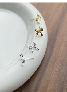 Détail de boucles d'oreilles nœuds élégantes en argent et or sur une assiette blanche